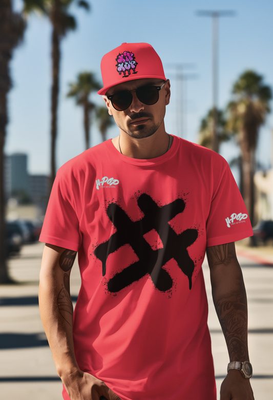 Un uomo con occhiali da sole e un berretto rosso con un'illustrazione fumettistica indossa una t-shirt rosso corallo. La maglietta ha una grande stampa centrale nera in stile graffito, che assomiglia a un asterisco o una forma astratta con un effetto gocciolante. L'uomo ha tatuaggi sulle braccia e un orologio al polso. Posa all'aperto in un ambiente urbano soleggiato con palme sullo sfondo.