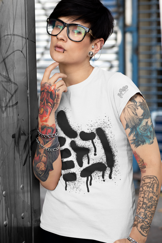 Una persona con capelli corti neri, occhiali da vista e piercing al viso e alle orecchie, indossa una maglietta bianca con una stampa grafica nera di forme astratte, simili a vernice spray o graffiti, con un effetto gocciolante. Le braccia della persona sono coperte da tatuaggi colorati. Si appoggia a una superficie verticale e guarda di lato, con una mano sul mento, in un ambiente urbano. La maglietta ha anche il logo "H-Pop" sulla manica.