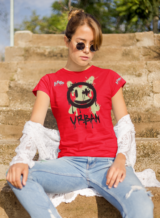 Giovane donna che indossa una maglietta rossa con stampa 'Urban' e faccina graffiti, seduta su scalini di pietra. Completa il look con jeans chiari, cardigan bianco e occhiali da sole rotondi. Ideale per abbigliamento streetwear femminile e moda urbana casual.