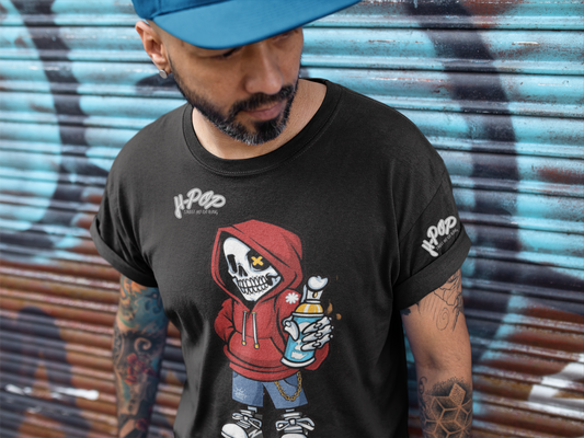 Un uomo con la barba e un cappellino da baseball blu indossato all'indietro indossa una maglietta nera con una stampa grafica di un personaggio scheletro cartoonesco che indossa una felpa con cappuccio rossa e jeans, con una bomboletta spray in mano e una catena. Lo scheletro ha un occhio a "X". La maglietta ha anche il logo "H-Pop" in alto a sinistra e sulla manica. L'uomo è in piedi con le braccia incrociate e guarda la maglietta, posando davanti a un muro di graffiti.
