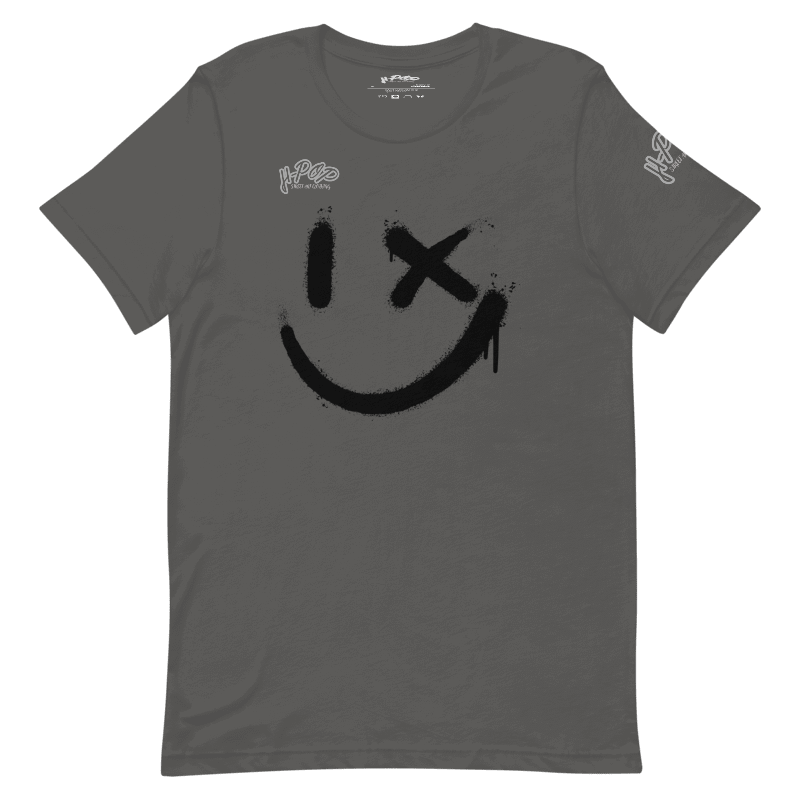 Una maglietta grigio scuro con una grande stampa nera di uno smiley stilizzato: un occhio è un tratto verticale e l'altro una "X", con un effetto vernice spray e gocciolante. La maglietta ha anche il logo "H-Pop" in alto a sinistra e sulla manica.