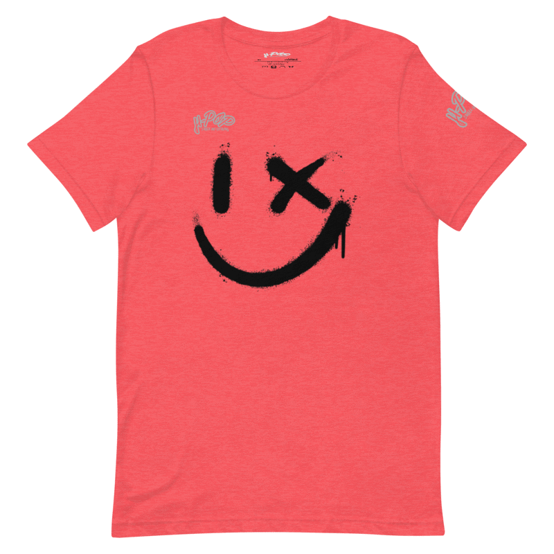 Una maglietta rosso corallo con una grande stampa nera di uno smiley stilizzato: un occhio è un tratto verticale e l'altro una "X", con un effetto vernice spray e gocciolante. La maglietta ha anche il logo "H-Pop" in alto a sinistra e sulla manica.