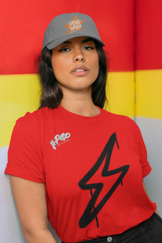 Donna con cappellino grigio e t-shirt rossa con fulmine nero in stile graffiti, su sfondo rosso e giallo. Un look audace e urbano, perfetto per chi ama lo streetwear. Parole chiave: t-shirt, maglietta, streetwear, moda, abbigliamento, donna, cappellino, fulmine, graffiti, urban, stile, tendenza, Italia.