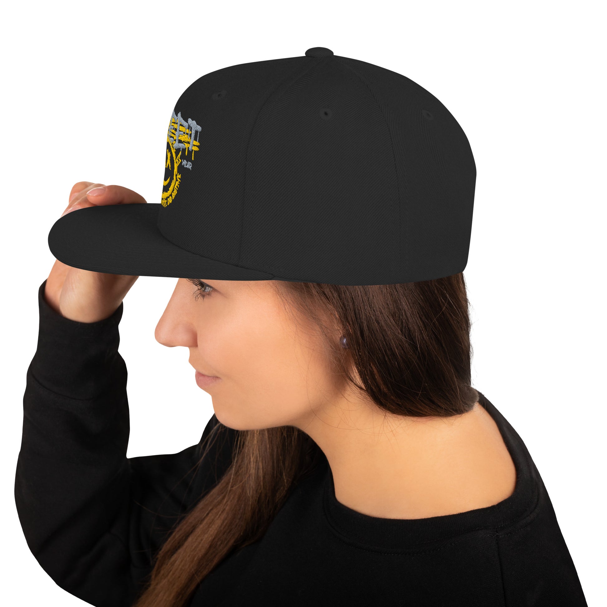 Donna di profilo che indossa un cappellino snapback nero con ricamo in stile graffiti: "STREETWEAR" in grigio e giallo, un volto sorridente giallo con occhi a "X" e la scritta circolare "KEEP SMILING BELIEVE AND SHINE". Ideale per abbigliamento urbano e accessori di tendenza. Parole chiave: cappellino, snapback, streetwear, graffiti, ricamo, moda donna, accessori, urban style, smile, nero, giallo, tendenza, Italia.