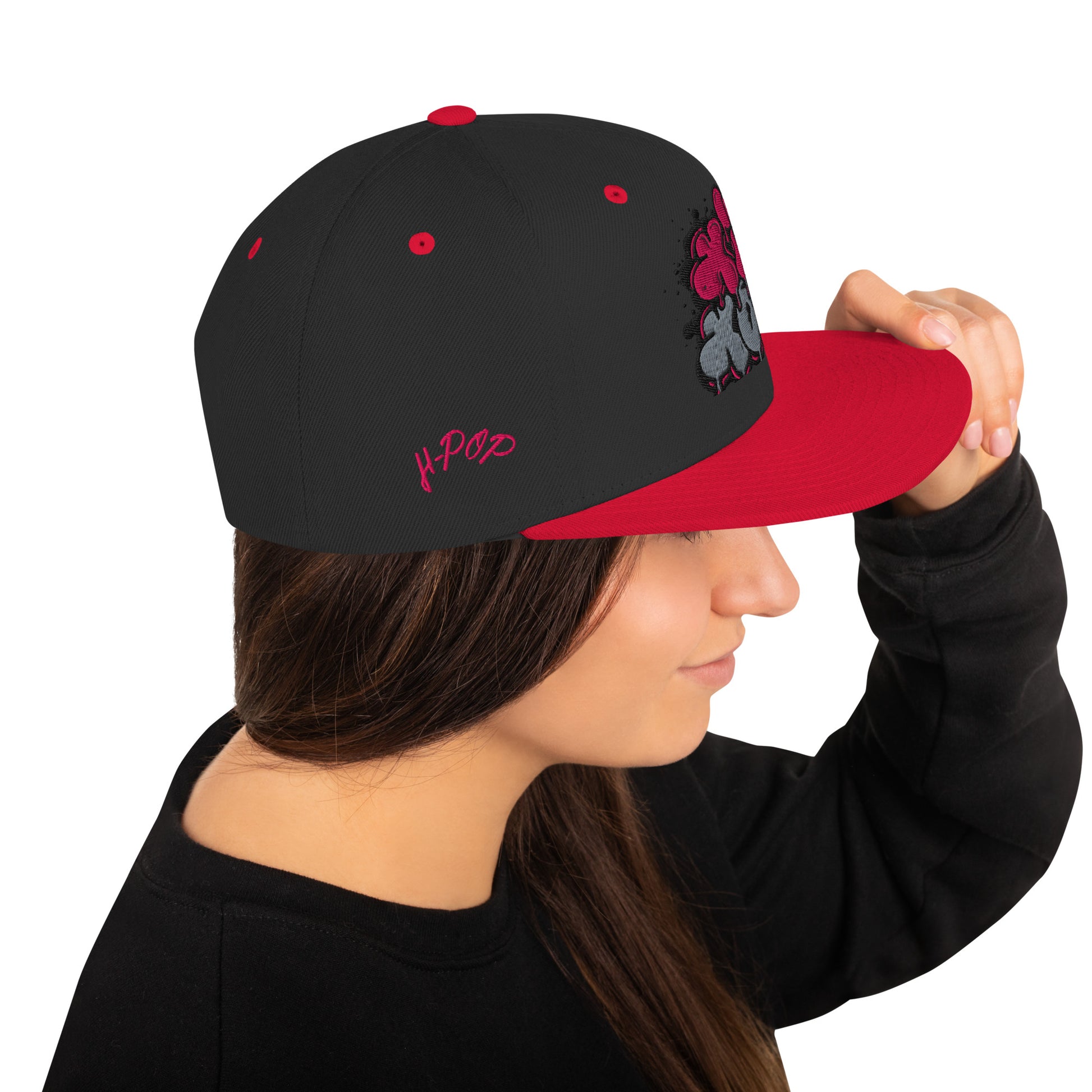 Profilo di una donna che indossa un cappellino snapback nero con visiera piatta rossa. Il cappellino presenta una stampa grafica in stile graffiti con la scritta 'Hip Hop' in rosa e grigio e il logo 'H-Pop' ricamato in rosa sul lato. Ideale per un look streetwear e audace. Parole chiave: cappellino, cappellino snapback, cappellino Hip Hop, streetwear, moda urbana, accessori moda, cappellino nero e rosso, stile graffiti, abbigliamento H-Pop, tendenze moda Italia.