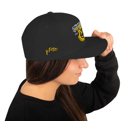 Donna di profilo che indossa un cappellino snapback nero con ricamo in stile graffiti: "STREETWEAR" in grigio e giallo, un volto sorridente giallo con occhi a "X" e la scritta circolare "KEEP SMILING BELIEVE AND SHINE" sul davanti, e il logo "H-Pop" ricamato in giallo sul lato. Ideale per abbigliamento urbano e accessori di tendenza. Parole chiave: cappellino, snapback, streetwear, graffiti, ricamo, moda donna, accessori, urban style, smile, nero, giallo, tendenza, Italia.