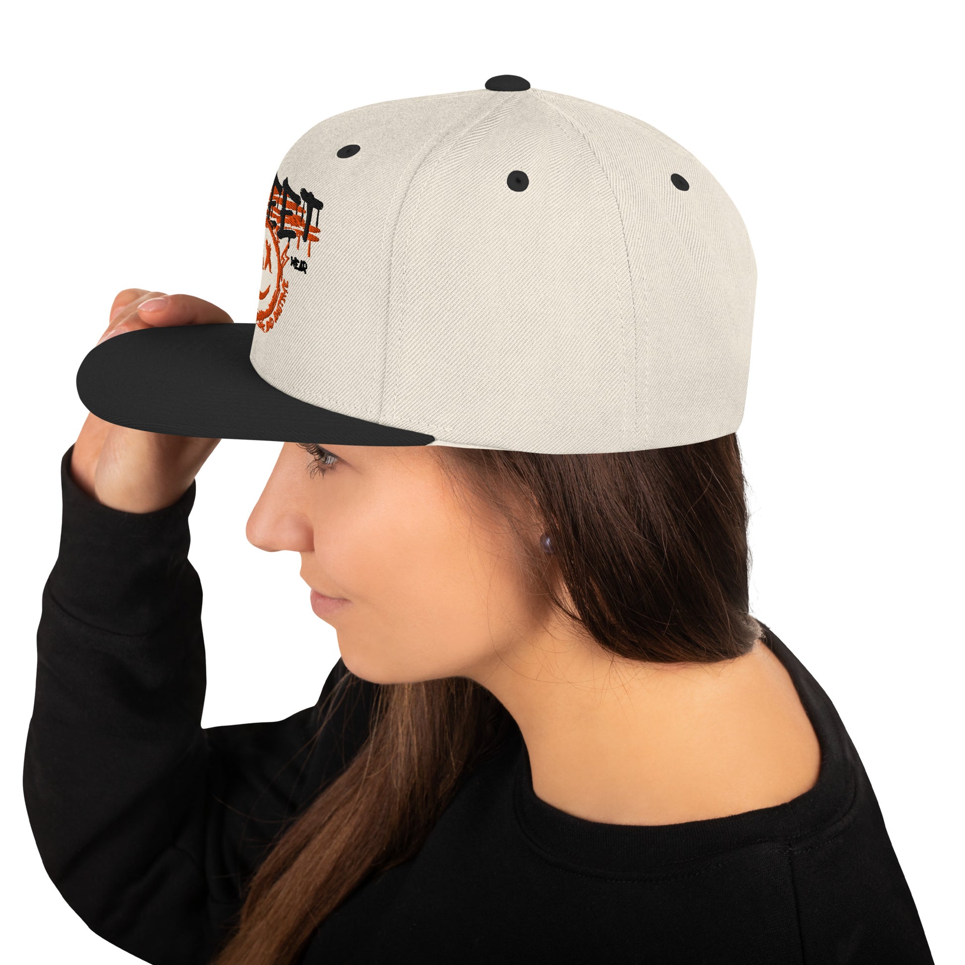 Profilo di una donna che indossa un cappellino snapback color crema con visiera piatta nera. Il cappellino presenta una grafica frontale con la scritta 'STREET' in arancione e un'emoji sorridente stilizzata. Perfetto per un look streetwear e casual. Parole chiave: cappellino, cappellino snapback, streetwear, moda casual, accessori moda, cappellino crema e nero, design grafico, abbigliamento urbano, tendenze moda Italia.