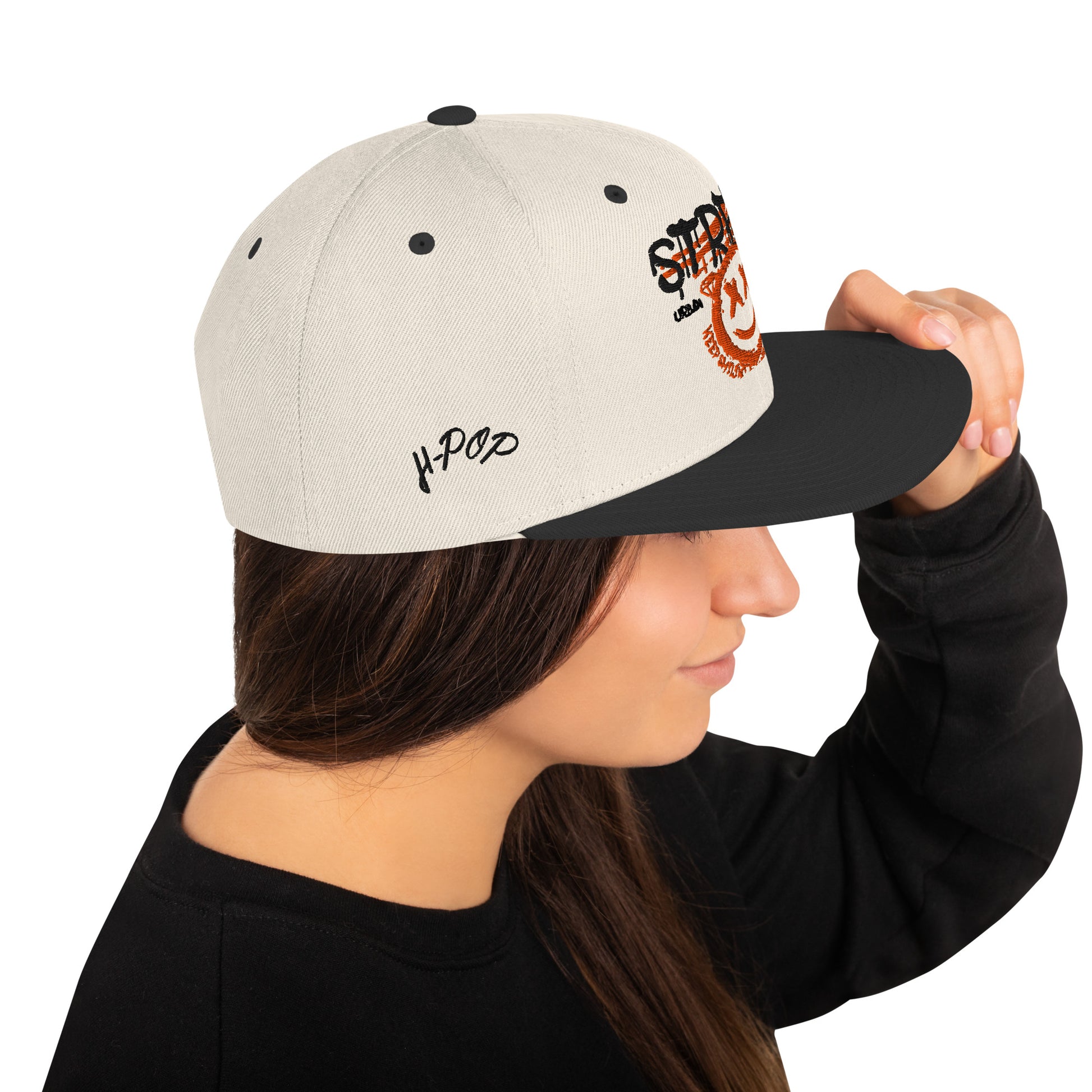 Profilo di una donna che indossa un cappellino snapback color crema con visiera nera. Il cappellino presenta una grafica frontale con la scritta 'STREET' e un'emoji sorridente con occhi a 'X', oltre al logo 'H-Pop' ricamato sul lato. Ideale per un look streetwear e urbano. Parole chiave: cappellino, cappellino snapback, streetwear, moda urbana, accessori moda, cappellino crema e nero, design grafico, abbigliamento H-Pop, tendenze moda Italia.