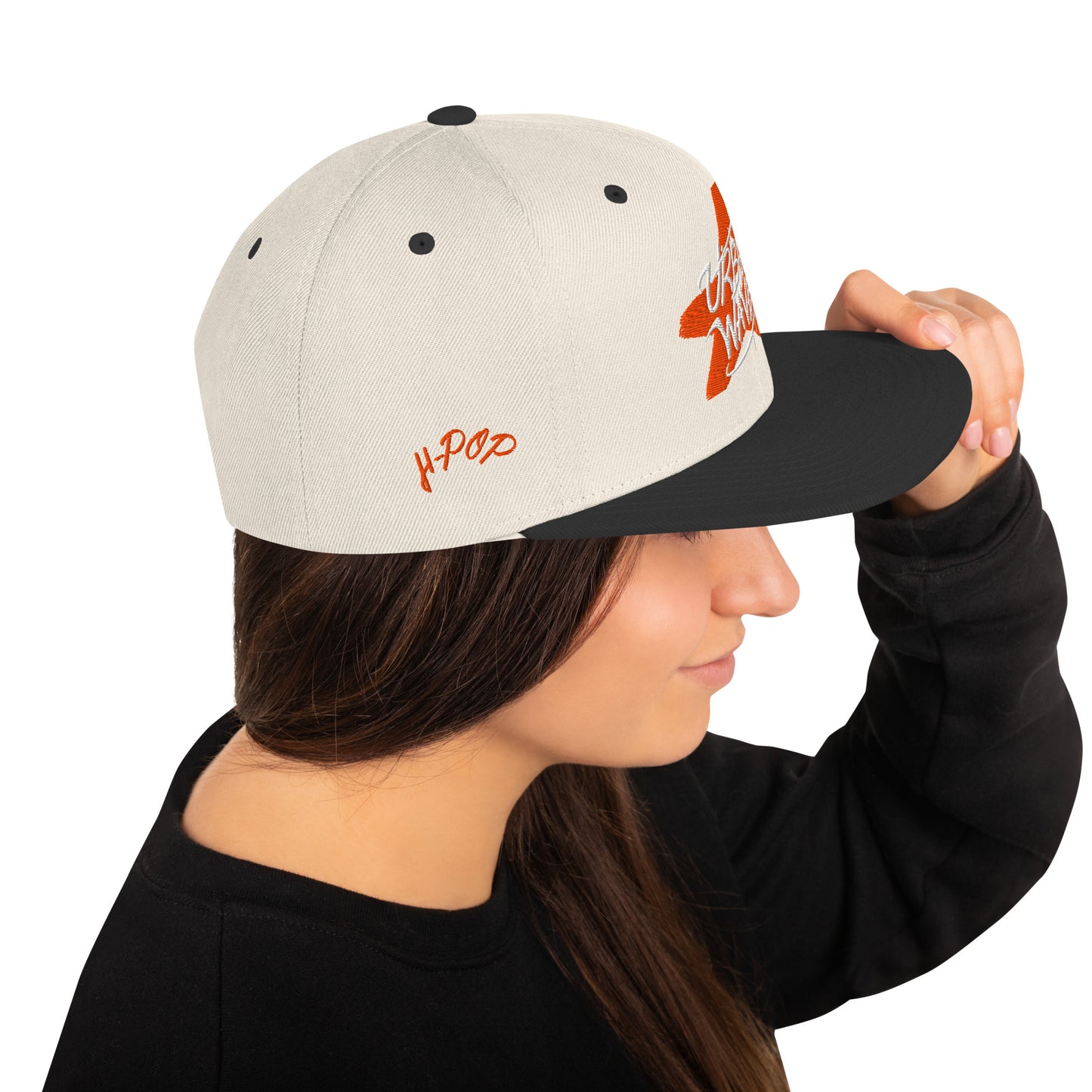 Donna di profilo che indossa un cappellino snapback bianco sporco con visiera nera, ricamato con una stella arancione stilizzata e la scritta "URBAN WAVES". Il logo "H-Pop" è ricamato in rosso sul lato. Ideale per un look streetwear e casual. Parole chiave: cappellino, snapback, bianco, nero, arancione, stella, urban, streetwear, moda donna, accessori, stile, tendenza, Italia.