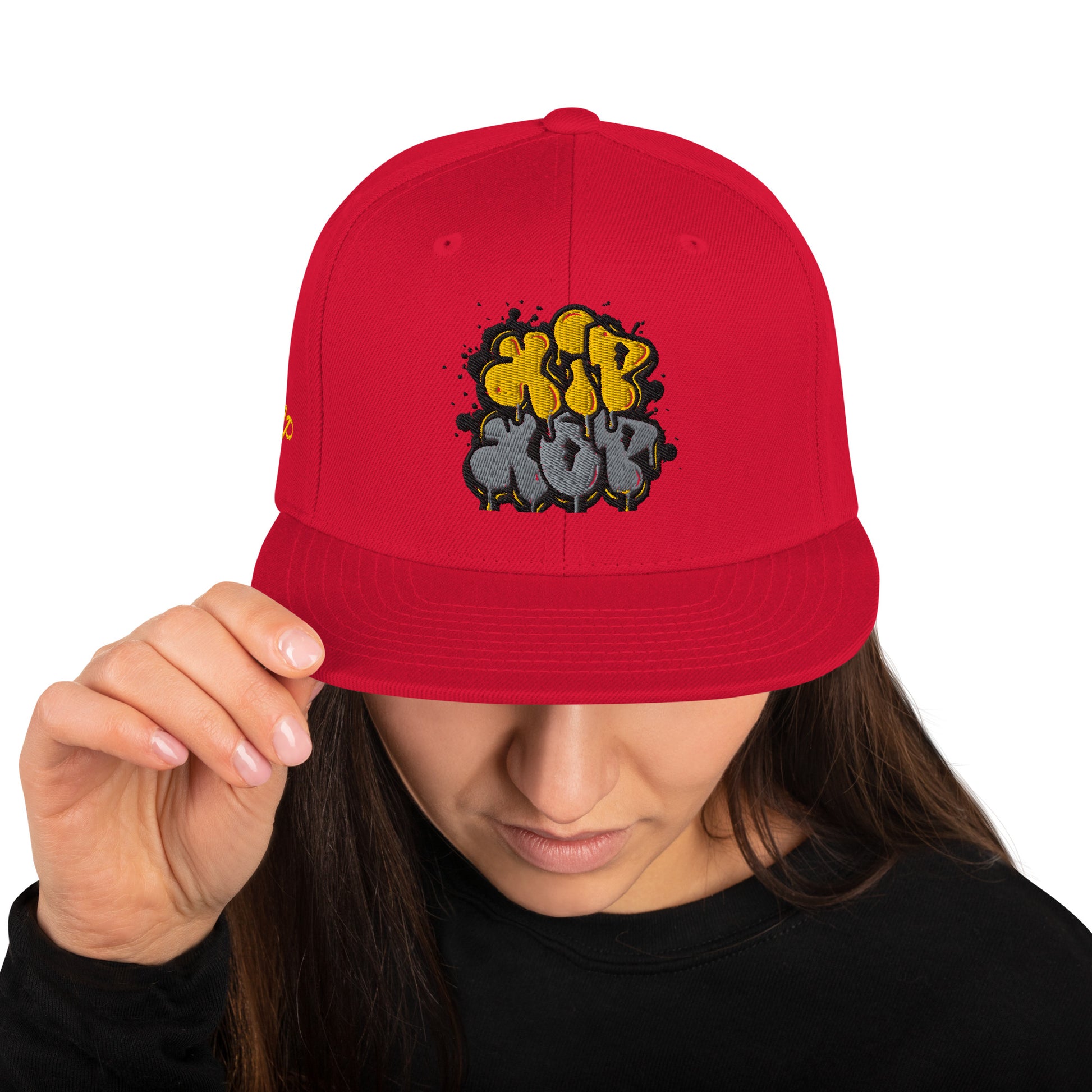 Persona che tiene un cappello snapback rosso con un logo 'Hip Hop' in stile graffiti giallo e grigio. Ideale per la moda streetwear, la cultura hip hop e gli accessori urbani di tendenza. Cappellino unisex con visiera piatta.